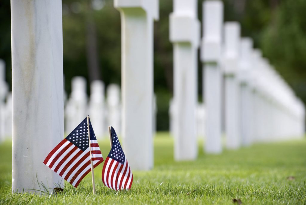 Two small American flags in front of white tombstone Two small American flags in front of white tombstone