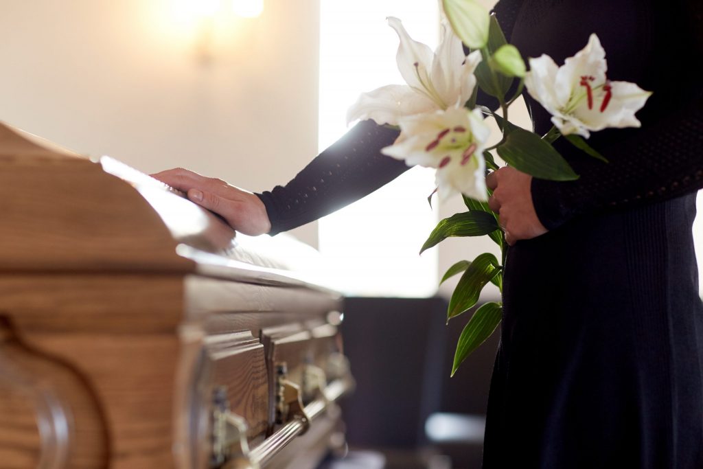Person holding flowers with their hand on a coffin at a funeral Person holding flowers with their hand on a coffin at a funeral